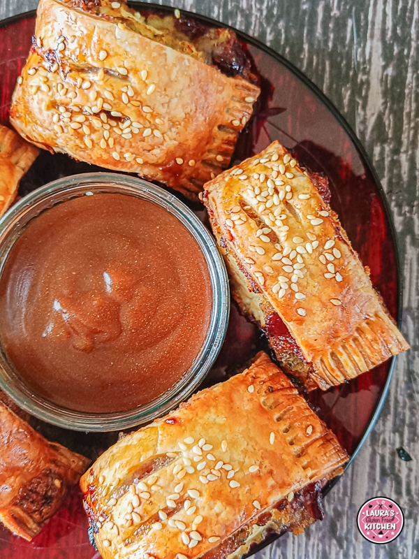 Baked golden-brown sausage rolls arranged around a dish of rich brown gravy on a red serving plate.
