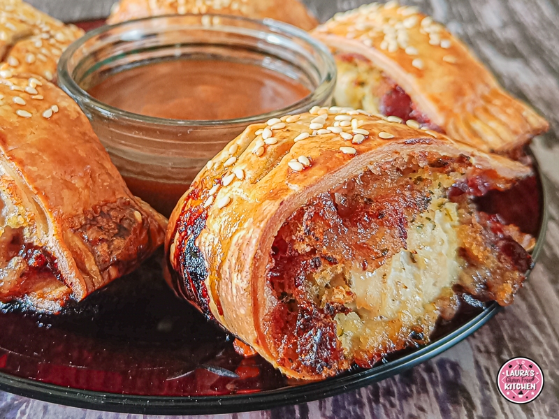 Baked golden-brown sausage rolls arranged around a dish of rich brown gravy on a red serving plate.