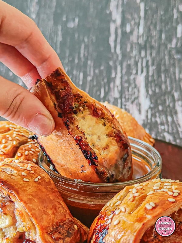Baked golden-brown sausage rolls arranged around a dish of rich brown gravy on a red serving plate.